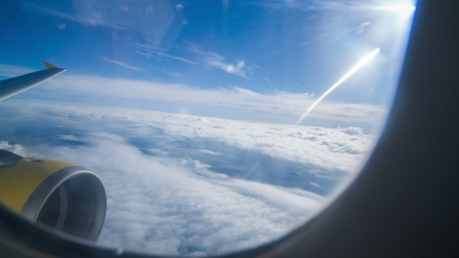 View from an airplane window of the wing, turbine, and clouds below on a sunny day